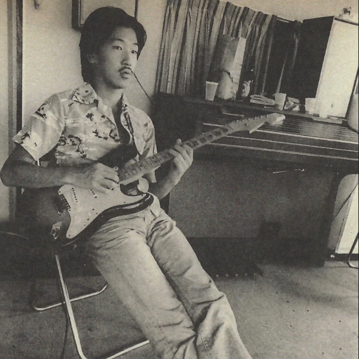 Black-and-white photo of Takanaka seated and playing an electric guitar